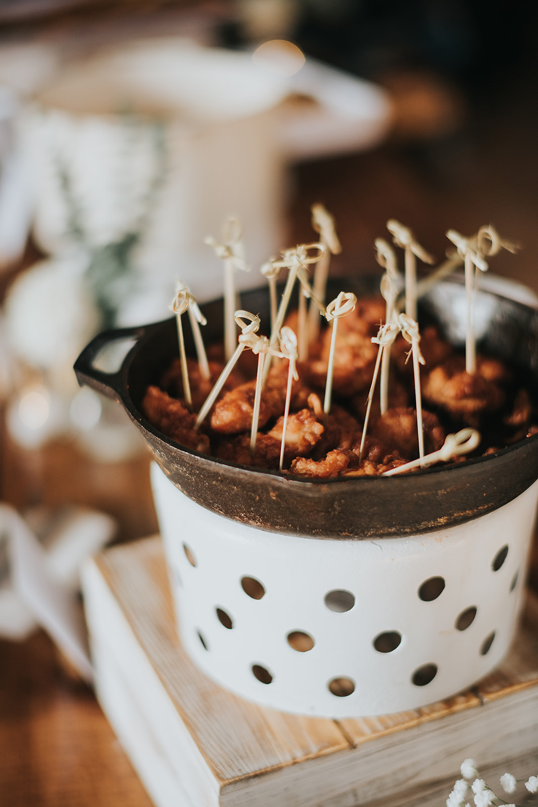 Close up of bite size chicken appetizers served in a white warming dish with bamboo skewers at a wedding cocktail hour at The Wells Estate.