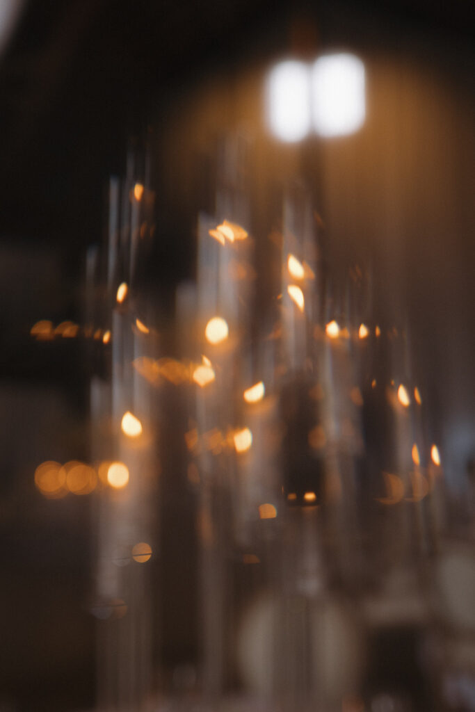 Close-up of glowing taper candles in glass cylinders creating a warm, romantic ambiance for an elegant wedding reception with soft bokeh lighting.