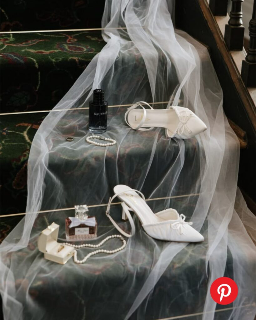 Wedding detail styling with white bridal heels, veil, perfume, and pearl jewelry arranged on a staircase for a romantic getting-ready moment.