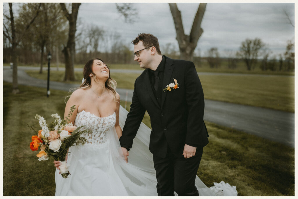 Bride and groom smiling and walking together outdoors holding hands during their wedding day.