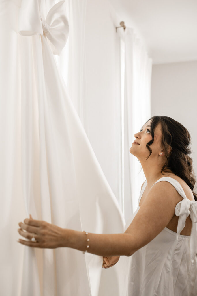 Bride admiring her wedding dress hanging in the bridal suite with soft light and neutral tones at The Wells Estate.