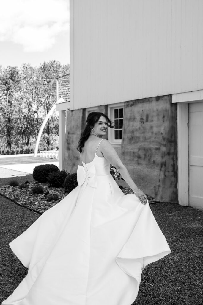 Bride spinning in a flowing wedding gown with a bow detail, captured outside near the barn at The Wells Estate.