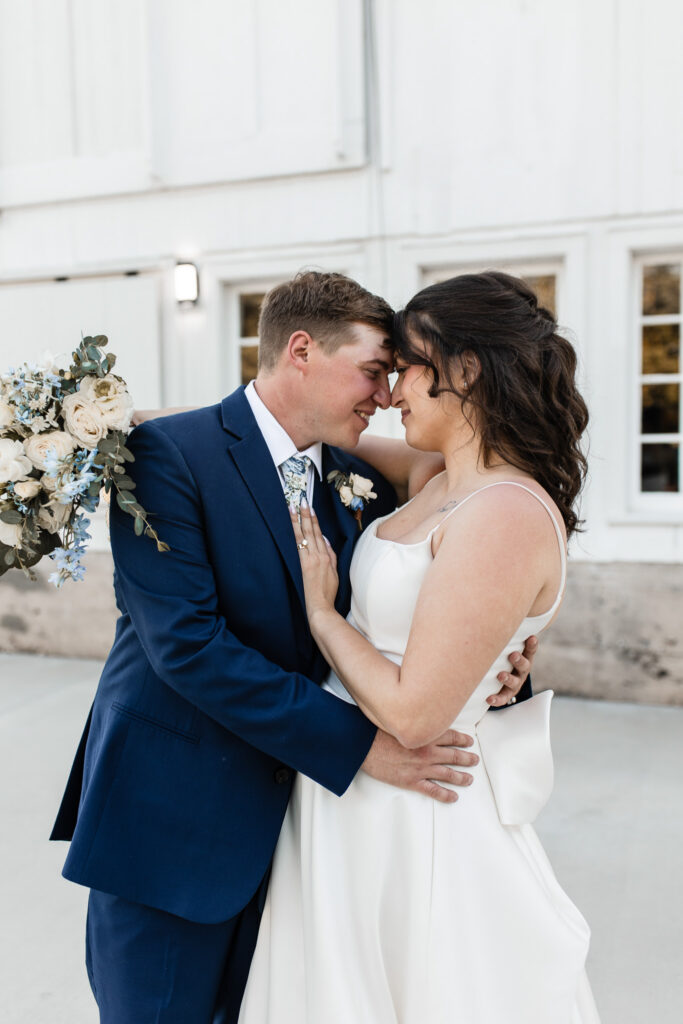 Bride and groom holding each other close outside the barn at The Wells Estate, soft florals and navy suit details.
