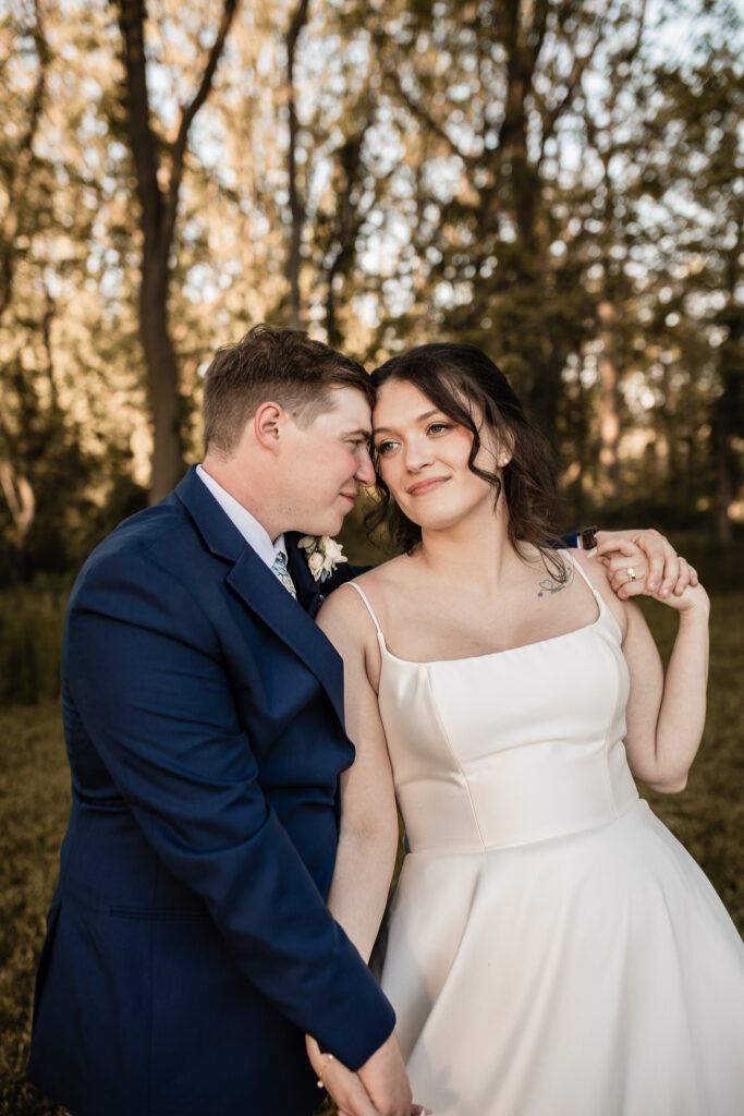 Bride and groom walking hand in hand through the trees at sunset, soft golden light at The Wells Estate.