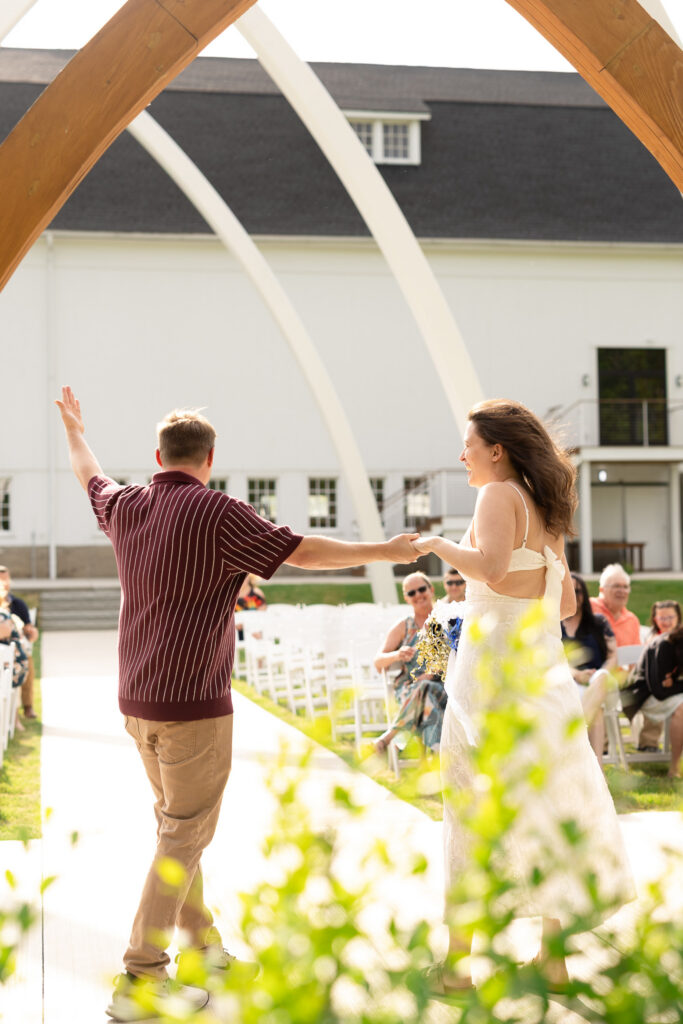 Couple standing close together for rehearsal beneath the Grand Arches ceremony space at The Wells Estate with rows of white chairs on either side.