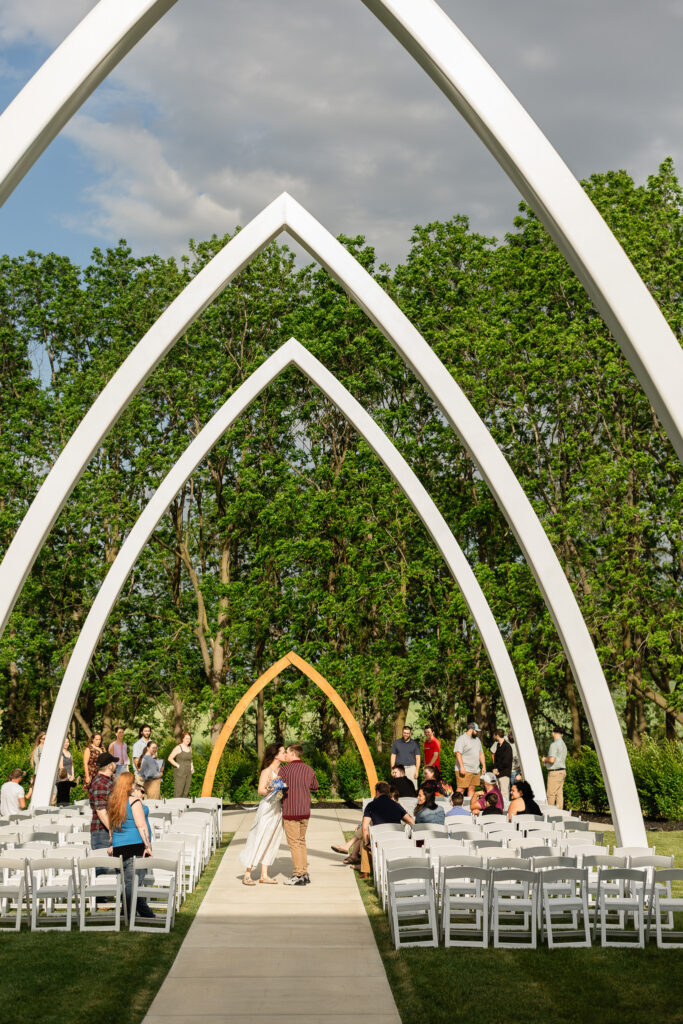 Wide view of the Grand Arches ceremony space at The Wells Estate with rows of white chairs and guests gathering before a rehearsal.