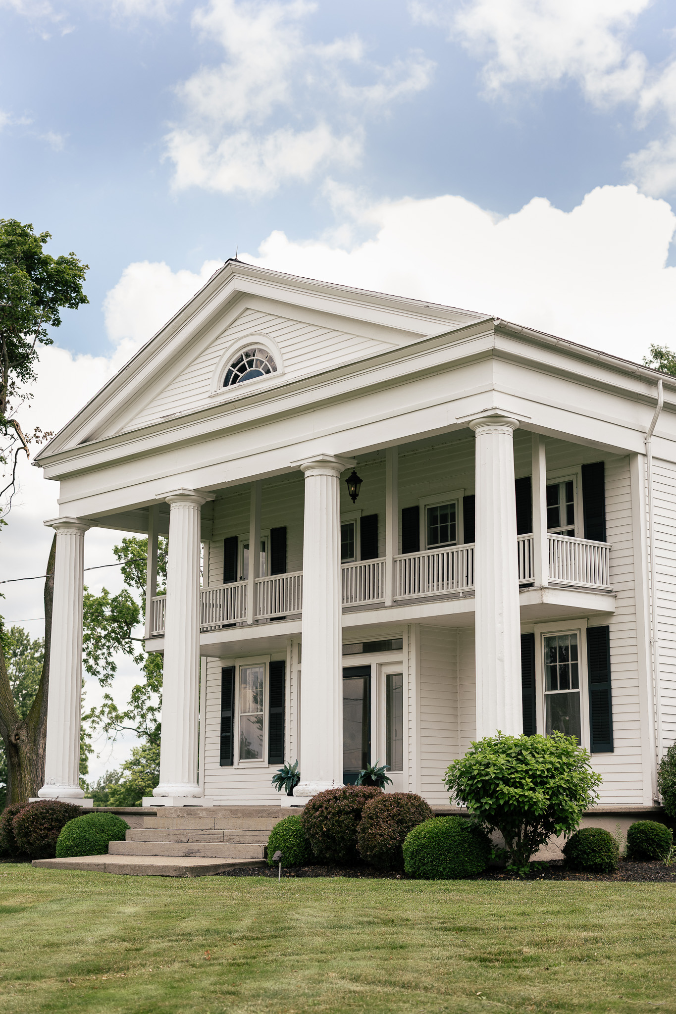 Front exterior of The Wells Estate House featuring grand white columns, a covered porch, and manicured landscaping at the wedding venue in Avon, New York.