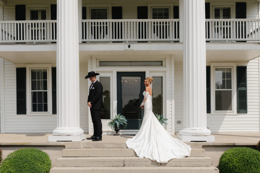 Bride and groom prepare for their first look on the front steps of the Estate House at The Wells Estate, framed by its signature white columns.