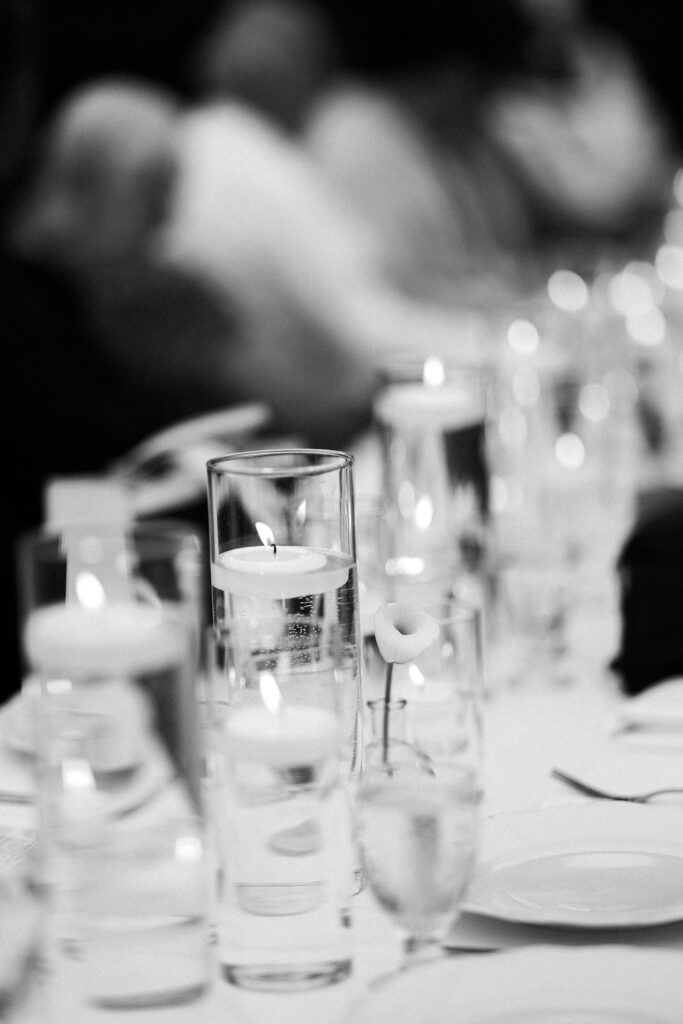 Black-and-white detail of glowing floating candles in glass cylinders creating a romantic candlelit wedding reception tablescape at The Wells Estate.