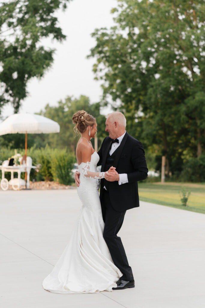 Bride shares a father-daughter dance during an outdoor wedding reception at The Wells Estate, surrounded by the estate’s greenery.