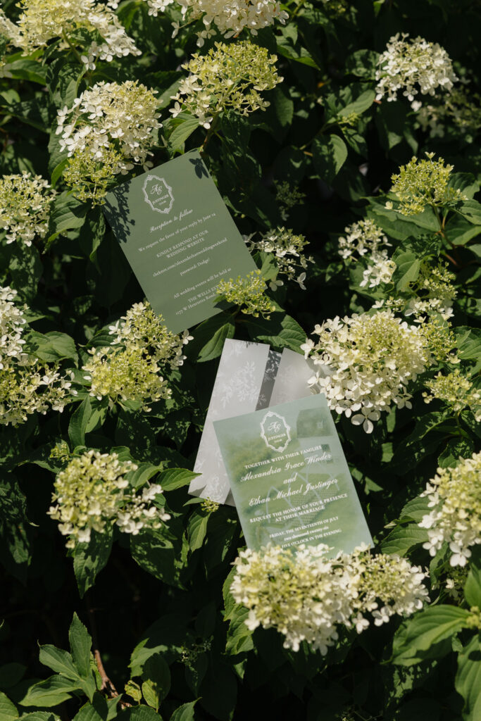 Green and white wedding invitation suite styled among blooming white hydrangeas for a summer wedding at The Wells Estate.