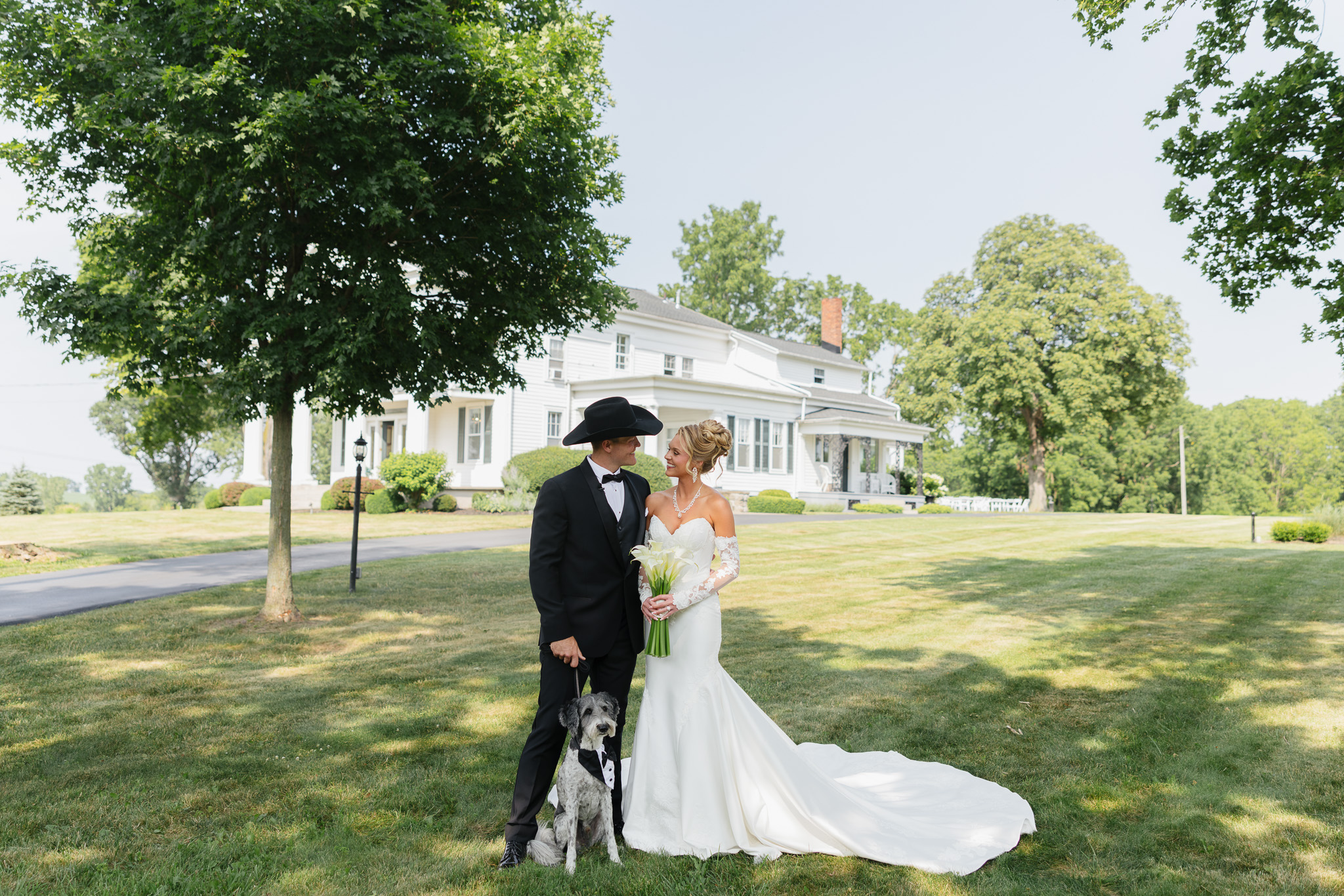 Bride and groom posing with their tuxedo-dressed dog on the lawn in front of the Estate House at The Wells Estate.