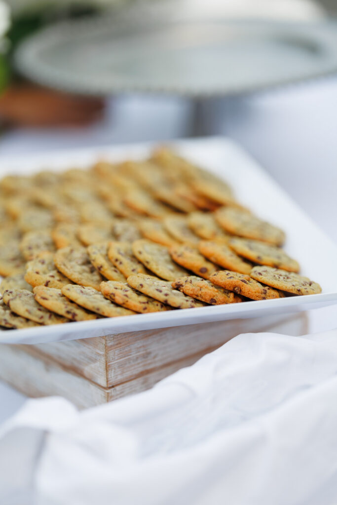 Trays of chocolate chip cookies displayed on a white and wood dessert station during a wedding reception at The Wells Estate.