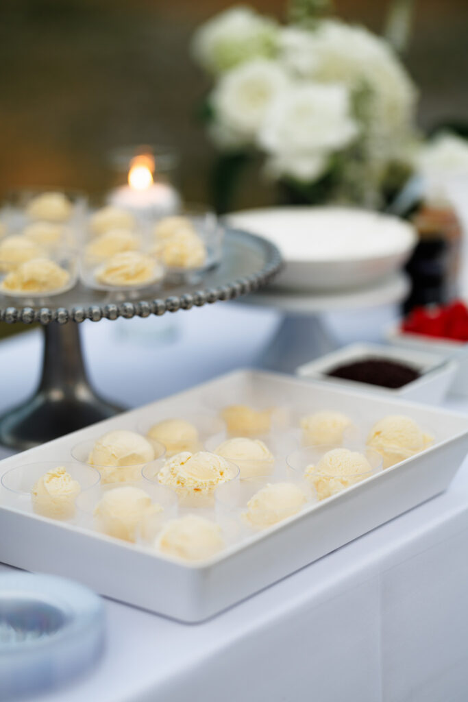 Individual scoops of vanilla ice cream arranged at an elegant dessert station with white florals and toppings during a wedding reception at The Wells Estate.